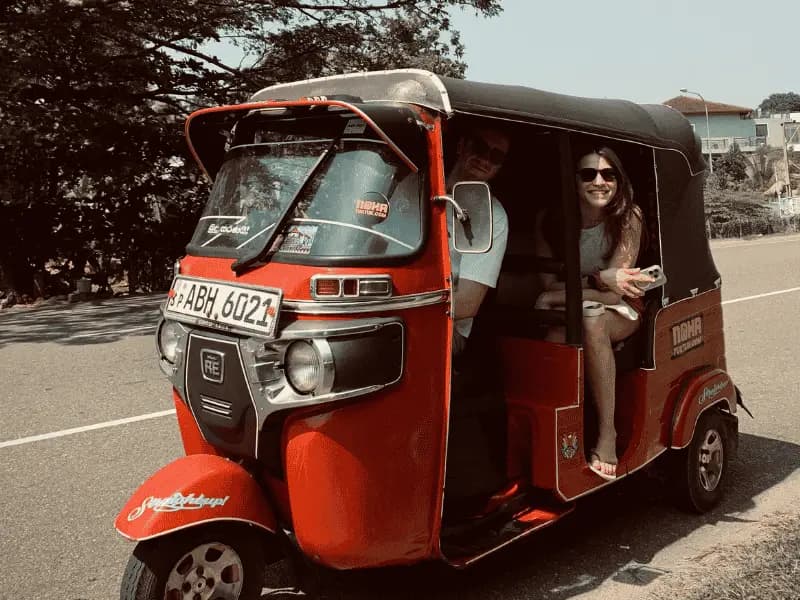 Two travellers driving a red NOHA self-drive tuk tuk on a coast road in Sri Lanka